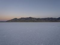 a lake with no water, in a mountainous plain at dusk with small mounds and mountains behind