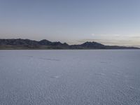 a lake with no water, in a mountainous plain at dusk with small mounds and mountains behind