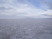 a white desert with mountains in the background and white clouds above it in the sky