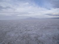 a white desert with mountains in the background and white clouds above it in the sky
