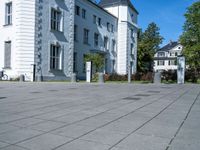 a person riding a bicycle down a sidewalk on a brick road near a white building