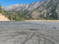 an empty parking lot in front of some hills with trees in the background with tracks in the pavement