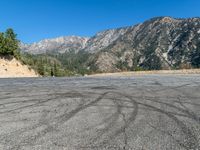 an empty parking lot in front of some hills with trees in the background with tracks in the pavement