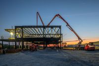 a picture of a building being built on a field near a forest in the background