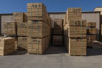 large group of wooden pallets stacked up outside of a warehouse building for sale, with some boxes and a man with a fork in handrail in the background