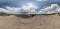 two people with skateboards on a dirt road under a cloudy blue sky and white clouds