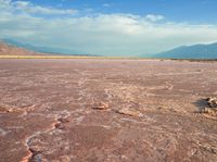 the large area of brown mud has a lone bench on the sand with mountains in the background