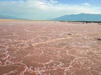 the large area of brown mud has a lone bench on the sand with mountains in the background