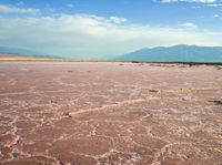 the large area of brown mud has a lone bench on the sand with mountains in the background