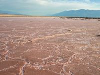 the large area of brown mud has a lone bench on the sand with mountains in the background