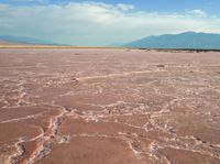 the large area of brown mud has a lone bench on the sand with mountains in the background