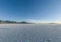 a wide expanse filled with snow and covered in mountains in the distance on a clear day