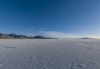 a wide expanse filled with snow and covered in mountains in the distance on a clear day