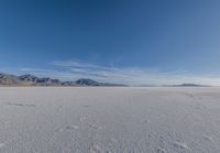 a wide expanse filled with snow and covered in mountains in the distance on a clear day