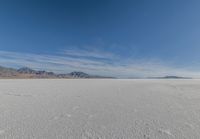 a wide expanse filled with snow and covered in mountains in the distance on a clear day