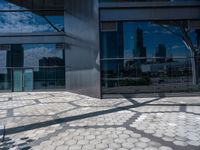 the outside of a building with a shadow of a tree on a pavement and there are skyscrapers in the distance