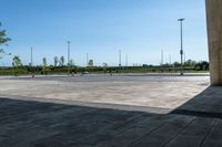 an empty parking lot with a few cars and people walking on it around it and buildings in the background