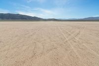 a sandy area with two mountains and sparse grass on the horizon in the distance is dirt that runs through the foreground