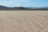 a sandy area with two mountains and sparse grass on the horizon in the distance is dirt that runs through the foreground