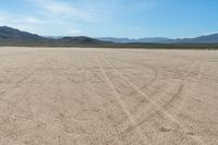 a sandy area with two mountains and sparse grass on the horizon in the distance is dirt that runs through the foreground