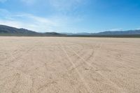 a sandy area with two mountains and sparse grass on the horizon in the distance is dirt that runs through the foreground