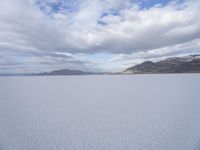 an empty desert field with large, wide expanses of snow and mountains in the distance