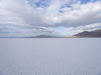 an empty desert field with large, wide expanses of snow and mountains in the distance