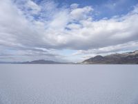 an empty desert field with large, wide expanses of snow and mountains in the distance