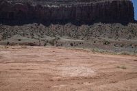 a dirt road through a desert plain with a mountain behind it and a clear blue sky in the background