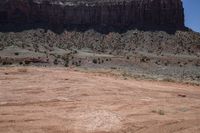 a dirt road through a desert plain with a mountain behind it and a clear blue sky in the background