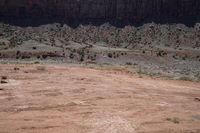 a dirt road through a desert plain with a mountain behind it and a clear blue sky in the background