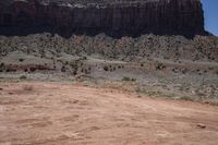 a dirt road through a desert plain with a mountain behind it and a clear blue sky in the background