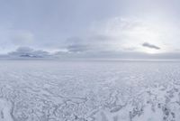an ocean is filled with clear ice floes with large mountains in the distance under a cloudy sky