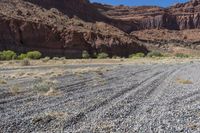 a dirt road lined by mountains and grass field area in front of rocky walls on a clear day