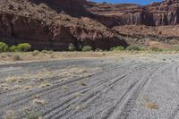 a dirt road lined by mountains and grass field area in front of rocky walls on a clear day