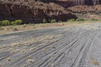 a dirt road lined by mountains and grass field area in front of rocky walls on a clear day