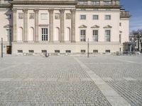 there are some people walking in front of the large building together, there is a square pavement