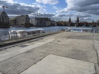 a concrete walkway that has a boat parked near it and a city across the river