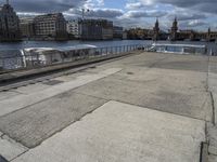 a concrete walkway that has a boat parked near it and a city across the river