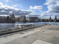 a concrete walkway that has a boat parked near it and a city across the river