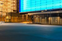 an empty parking lot and a very tall building lit up blue in the night sky