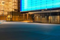 an empty parking lot and a very tall building lit up blue in the night sky