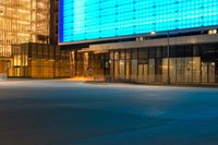 an empty parking lot and a very tall building lit up blue in the night sky