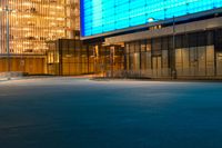 an empty parking lot and a very tall building lit up blue in the night sky