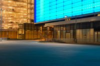 an empty parking lot and a very tall building lit up blue in the night sky