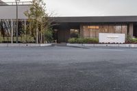 a man skateboarding along a paved parking area outside a building with landscaping and trees