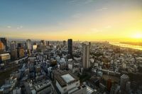 the sun sets behind tall buildings on a city street with many cars passing through the road