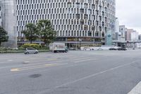 a car driving down a city street past a tall building, with many cars parked along it