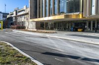 street sign sitting next to grass and sidewalk in front of building with windows and parking lot behind it