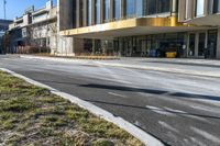 street sign sitting next to grass and sidewalk in front of building with windows and parking lot behind it